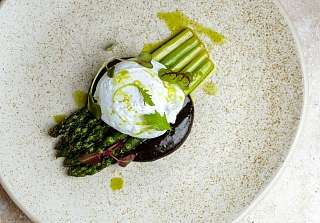 Piatto primaverile con asparagi verdi e bianchi, uovo in camicia e olio alle erbe, presentato con eleganza.