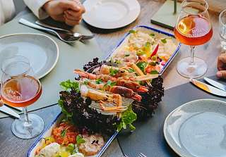 Meeresfrüchte-Platte mit gegrillten Garnelen, Lachs-Tatar, Hummus und frischen Kräutern auf einem gedeckten Tisch mit Bier-Gläsern